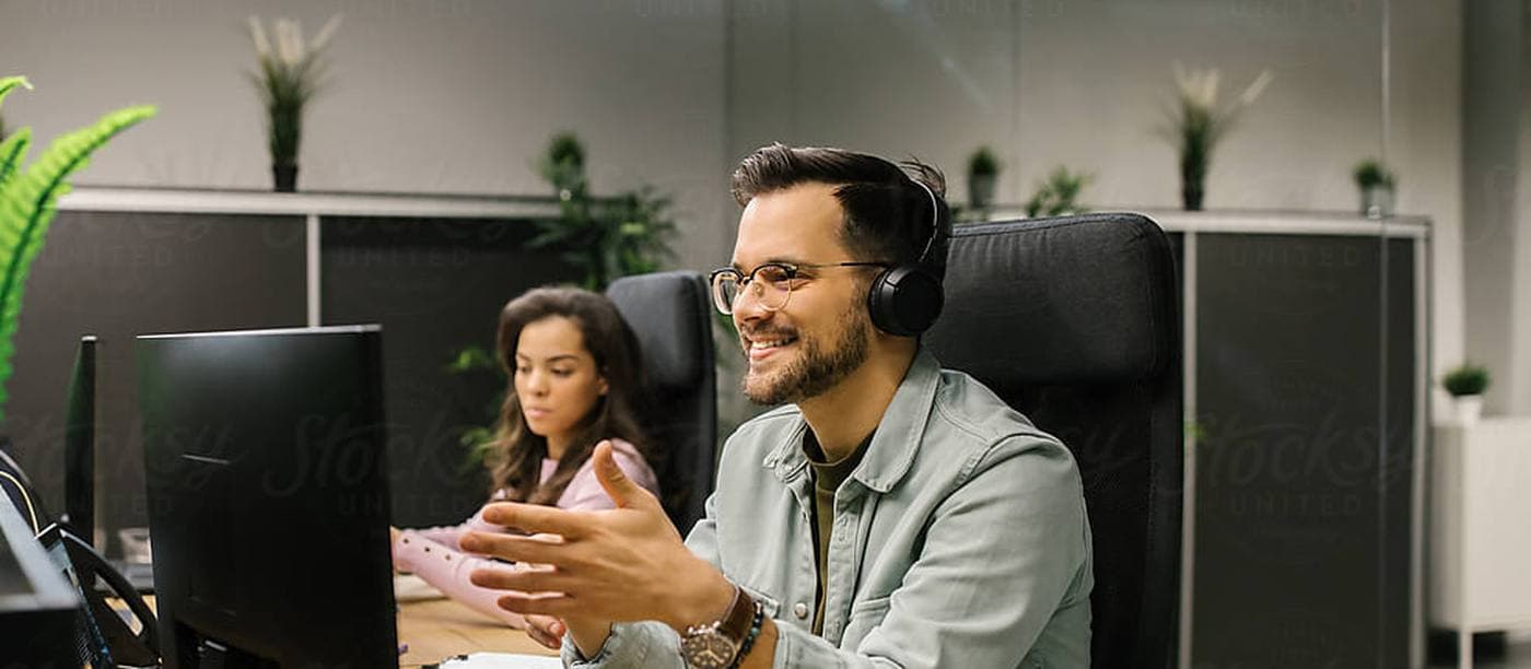 A coordinator in a headset working at a desk with a colleague behind him